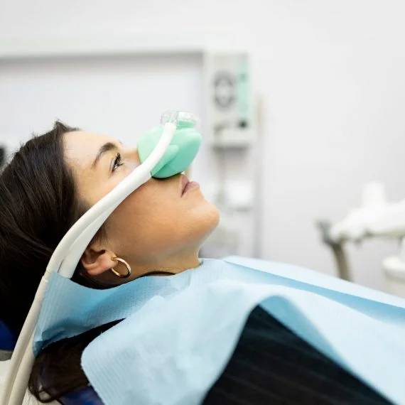 Woman tilting back in dental chair receiving nasal sedation mask for comfortable dental treatment